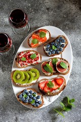 Healthy vegetarian sandwiches made from rye bread with soft cheese, organic berries and fruits - strawberries, blueberries, kiwi, figs, pomegranate seeds and mint.