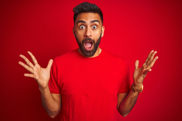 Young handsome indian man wearing t-shirt over isolated red background celebrating crazy and amazed...