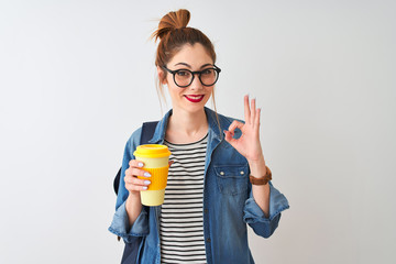 Beautiful redhead student woman drinking take away coffee over isolated white background doing ok sign with fingers, excellent symbol