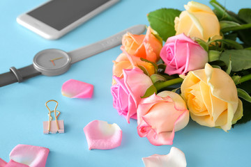 Beautiful rose flowers with mobile phone and watch on color background