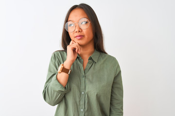 Young chinese woman wearing green shirt and glasses over isolated white background with hand on chin thinking about question, pensive expression. Smiling with thoughtful face. Doubt concept.