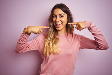 Young beautiful woman wearing a sweater over pink isolated background smiling cheerful showing and pointing with fingers teeth and mouth. Dental health concept.