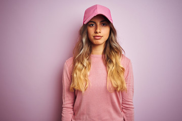 Young beautiful woman wearing cap over pink isolated background with serious expression on face. Simple and natural looking at the camera.