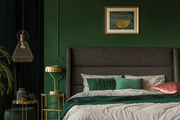 Stylish emerald green and golden poster above comfortable king size bed with headboard and pillows...