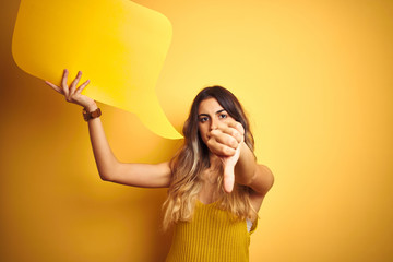 Young beautiful woman holding speech bubble over yellow isolated background with angry face,...