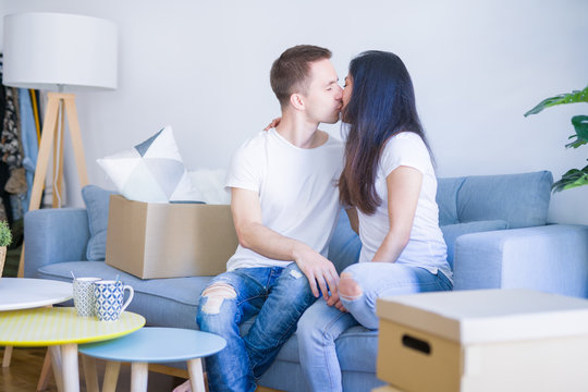 Young beautiful couple sitting on the sofa drinking coffee at new home around cardboard boxes
