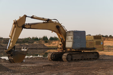 Excavator on the shore of a sand pit turning into a pond.
