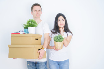 Young beautiful couple holding cardboard boxes standing over isolated white background serious face...
