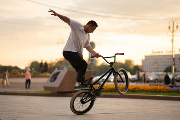 The guy performs a stunt on BMX, standing on the rear wheel.