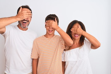 Family of three, mother, father and son standing over white isolated background smiling and laughing with hand on face covering eyes for surprise. Blind concept.