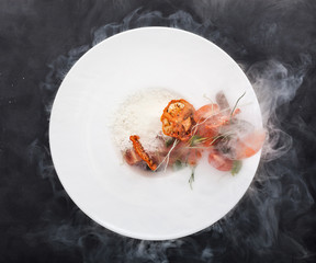 Vegan white rice with fresh and dried tomatoes with smoke on a plate. Top view over black background.
