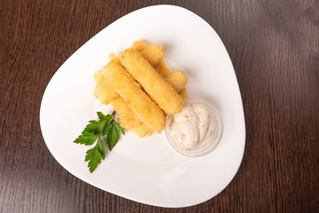 Cheese sticks breaded, with sauce and herbs, on a platter.