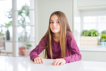 Beautiful young girl kid on white table Relaxed with serious expression on face. Simple and natural looking at the camera.