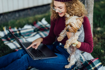 Student woman sitting on the blanket and have a picnic time with her Yorkshire terrier dog. Look at...