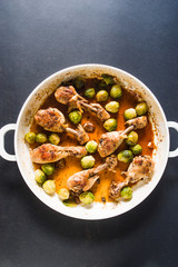 Roasted chicken legs in pan cooked with beer, with bruxelles sprout on a white ceramic pan, top view on a wooden backgorund white color, flatlay