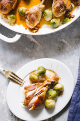 Roasted chicken legs in pan cooked with beer, with bruxelles sprout on a white ceramic pan, top view on a wooden backgorund white color, flatlay