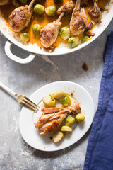Roasted chicken legs in pan cooked with beer, with bruxelles sprout on a white ceramic pan, top view on a wooden backgorund white color, flatlay