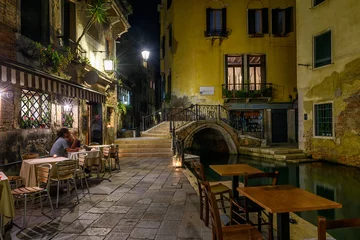 Foto op Plexiglas Smalle gracht met brug en tafels van restaurant in Venetië, Italië. Architectuur en mijlpaal van Venetië. Nacht gezellige stadsgezicht van Venetië. © Ekaterina Belova