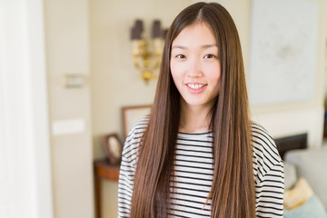 Beautiful Asian woman wearing stripes sweater over living room background with a happy and cool smile on face. Lucky person.
