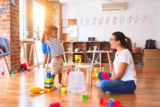 Beautiful teacher and toddler boy playing drum using skitlle and plastic basket at kindergarten