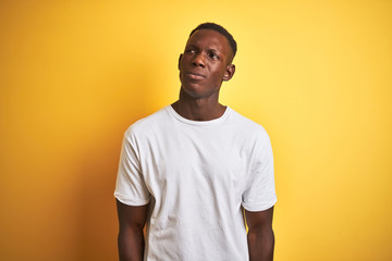Young african american man wearing white t-shirt standing over isolated yellow background smiling looking to the side and staring away thinking.