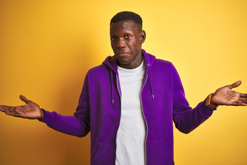African american man wearing purple sweatshirt standing over isolated yellow background clueless...