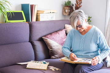 An attractive senior lady looking at her old stamps collection. Sitting on sofa with cellphone and tablet. White wall and books on background - Powered by Adobe
