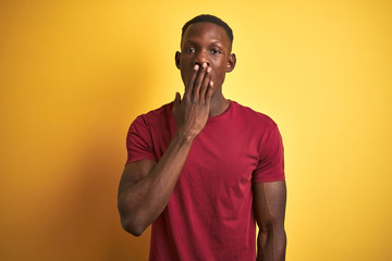 Young african american man wearing red t-shirt standing over isolated yellow background bored yawning tired covering mouth with hand. Restless and sleepiness.