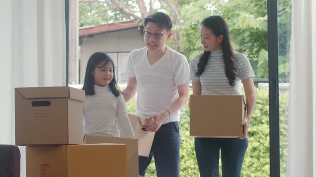 Happy Asian young family bought new house. Japanese Mom, Dad, and child smiling happy hold cardboard boxes for move object walking into big modern home. New real estate dwelling, loan and mortgage.