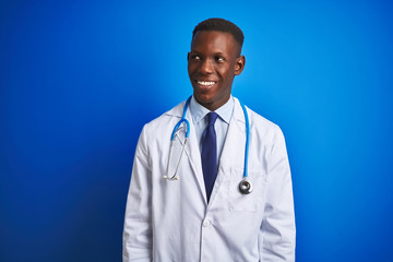 Fototapeta premium African american doctor man wearing stethoscope standing over isolated blue background looking away to side with smile on face, natural expression. Laughing confident.