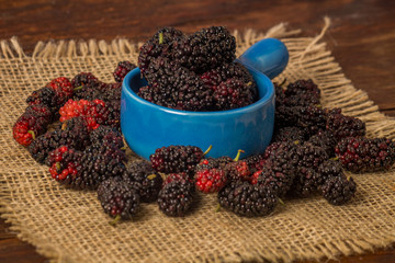Fresh blackberries on wooden table in a blue bowl with a rustic jute.