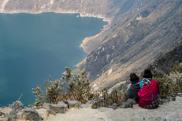 Ecuadorian women, with their traditional clothes, admire the spectacular Quilotoa lake at over 3500...