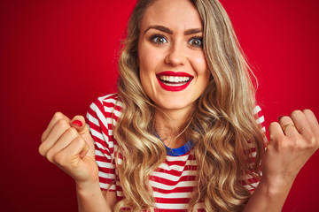 Young beautiful woman wearing stripes t-shirt standing over red isolated background screaming proud and celebrating victory and success very excited, cheering emotion
