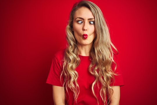 Young beautiful woman wearing basic t-shirt standing over red isolated background making fish face with lips, crazy and comical gesture. Funny expression.
