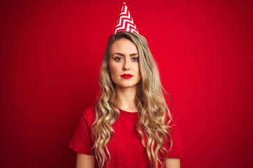 Young beautiful woman wearing bitrhday hat over red isolated background with a confident expression on smart face thinking serious