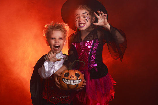 happy children girl and boy in costumes of witch and vampire in dark red background in halloween.