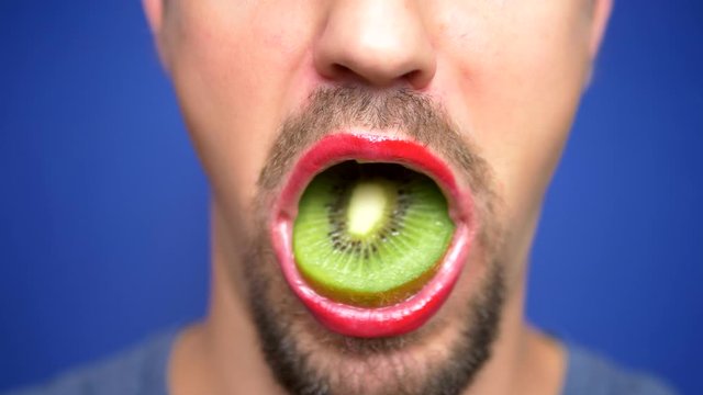 close-up. funny image of a bearded man with lip make-up holding a kiwi in his mouth
