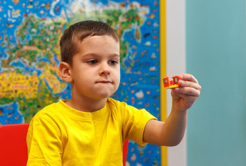 Little kid boy in yellow t-shirt playing with lots of colorful plastic blocks indoor. Child having fun with building and creating
