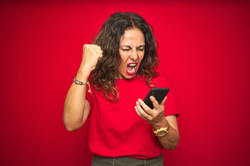Naklejka premium Middle age senior woman using smartphone over red isolated background annoyed and frustrated shouting with anger, crazy and yelling with raised hand, anger concept
