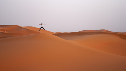 A cheerful girl is jumping on top of a sand dune in the Sahara desert, vacation in Morocco.