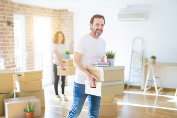 Fototapeta na wymiar Middle age senior couple moving to a new house, man smiling happy in love with new apartment and holding cardboard boxes
