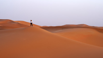 Fototapeta na wymiar Female traveler stands on top of a sand dune in the Sahara desert, vacation in Morocco.