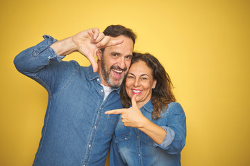 Obraz premium Beautiful middle age couple together standing over isolated yellow background smiling making frame with hands and fingers with happy face. Creativity and photography concept.