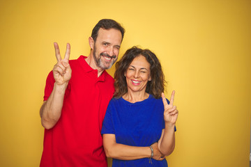 Beautiful middle age couple together standing over isolated yellow background smiling with happy...