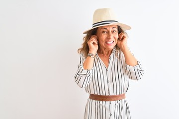 Obraz na płótnie Canvas Middle age businesswoman wearing striped dress and hat over isolated white background covering ears with fingers with annoyed expression for the noise of loud music. Deaf concept.