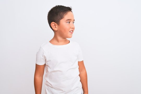 Beautiful kid boy wearing casual t-shirt standing over isolated white background looking away to side with smile on face, natural expression. Laughing confident.