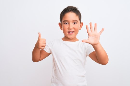 Beautiful kid boy wearing casual t-shirt standing over isolated white background showing and pointing up with fingers number six while smiling confident and happy.