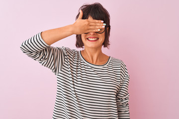 Young beautiful woman wearing striped t-shirt and glasses over isolated pink background smiling and laughing with hand on face covering eyes for surprise. Blind concept.