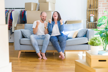Fototapeta na wymiar Young couple sitting on the sofa arround cardboard boxes moving to a new house very happy and excited doing winner gesture with arms raised, smiling and screaming for success. Celebration concept.