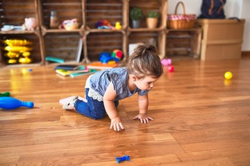 Beautiful toddler crawling on the floor around lots of toys at kindergarten